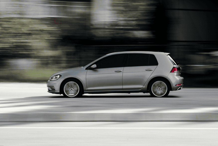 Carro hatch prata em alta velocidade em área urbana desfocada ao fundo.