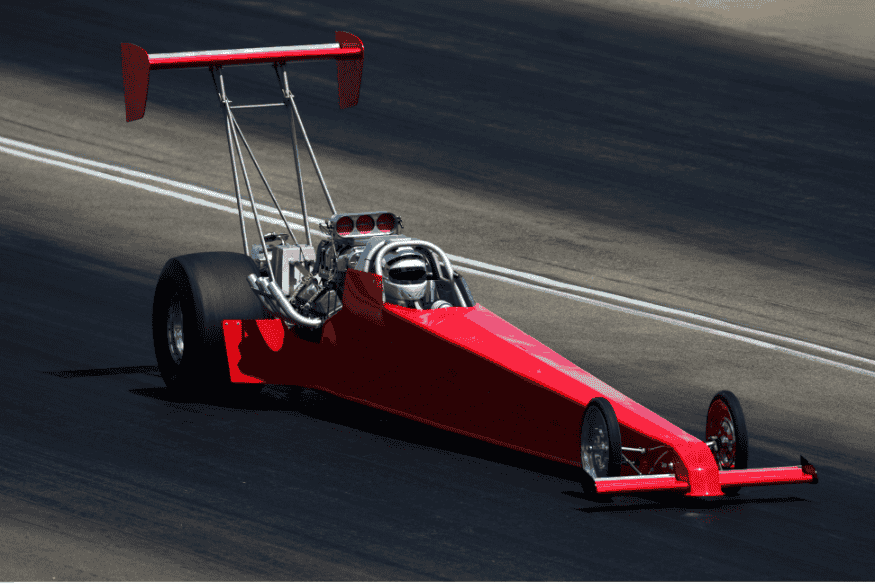 Dragster vermelho com estrutura aerodinâmica e motor exposto acelerando em pista de arrancada.