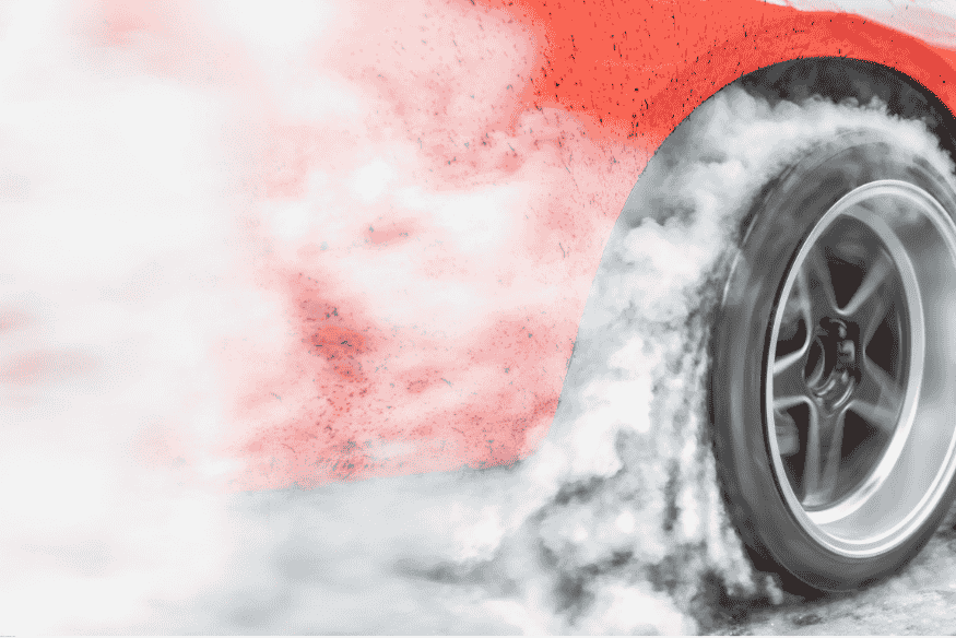 Detalhe de pneu traseiro de carro de arrancada queimando borracha com grande volume de fumaça.