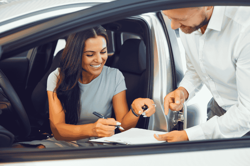 Mulher assinando contrato de consórcio automotivo dentro do veículo com vendedor ao lado.