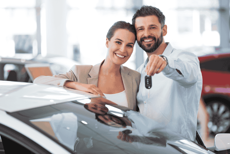 Casal feliz em concessionária mostrando chave de carro novo após aquisição segura.