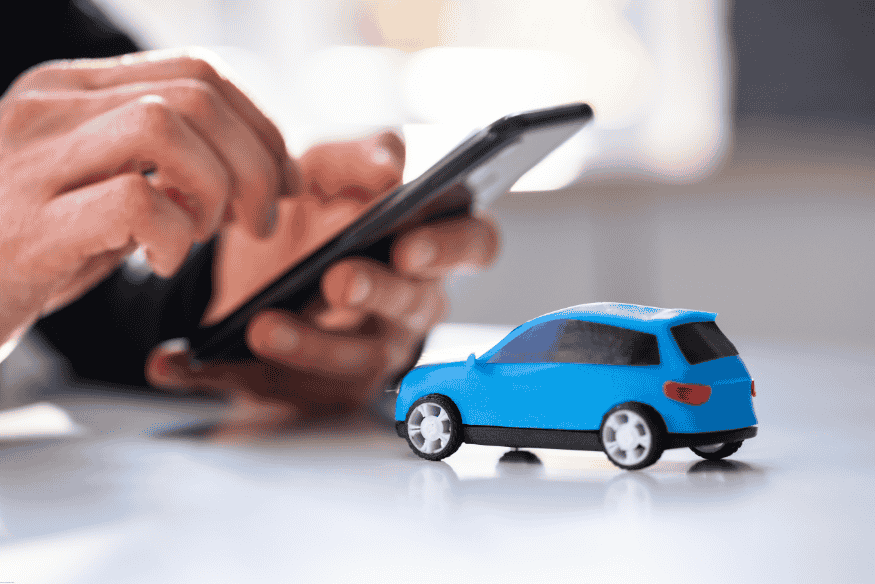 Pessoa usando celular ao lado de um carro em miniatura, simbolizando compra de carro por consórcio online.