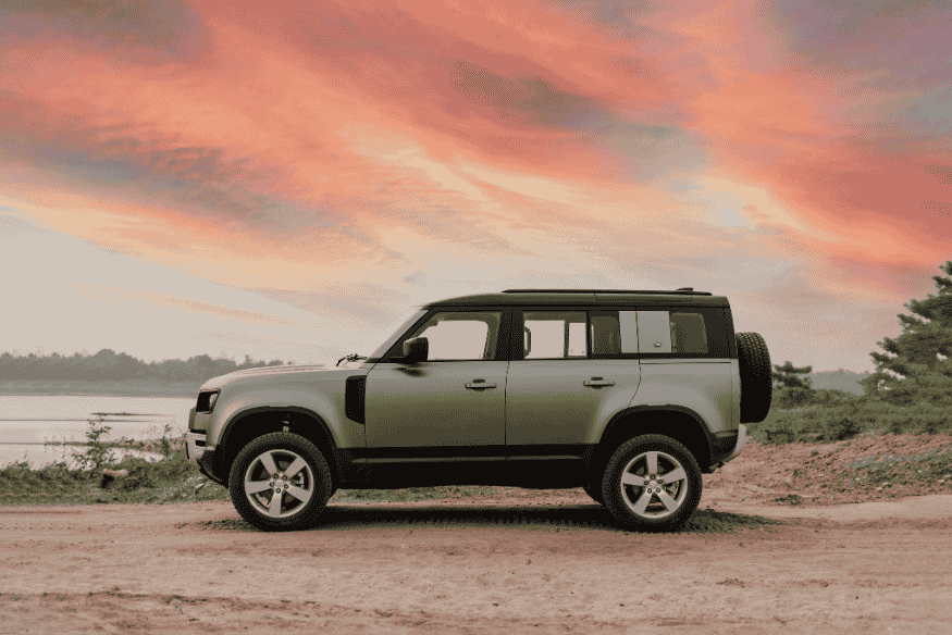 SUV com tração integral estacionado em estrada de terra ao pôr do sol, próximo a lago.