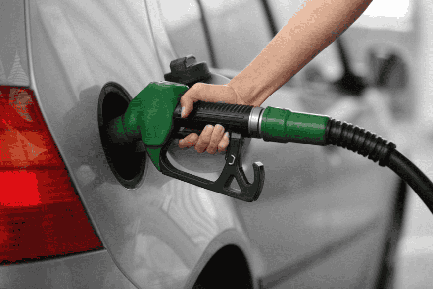 Pessoa abastecendo um carro prata com bomba de combustível do lado direito