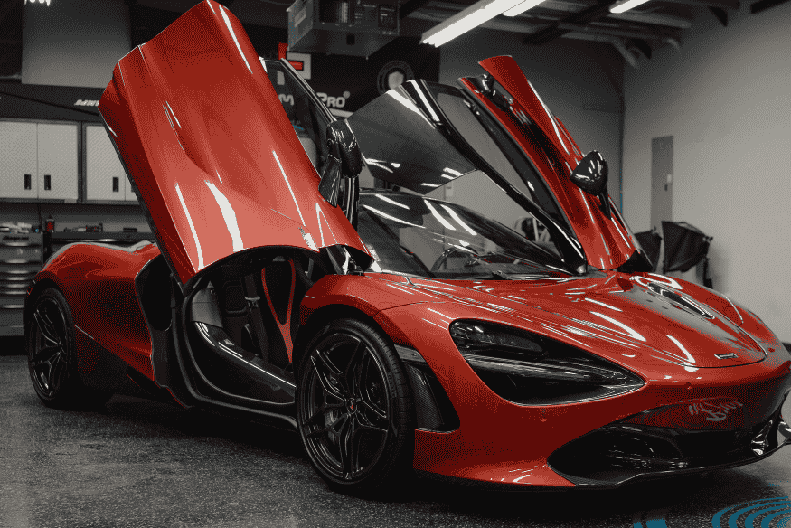 Carro esportivo vermelho com portas abertas em estilo borboleta, estacionado em garagem de alto padrão