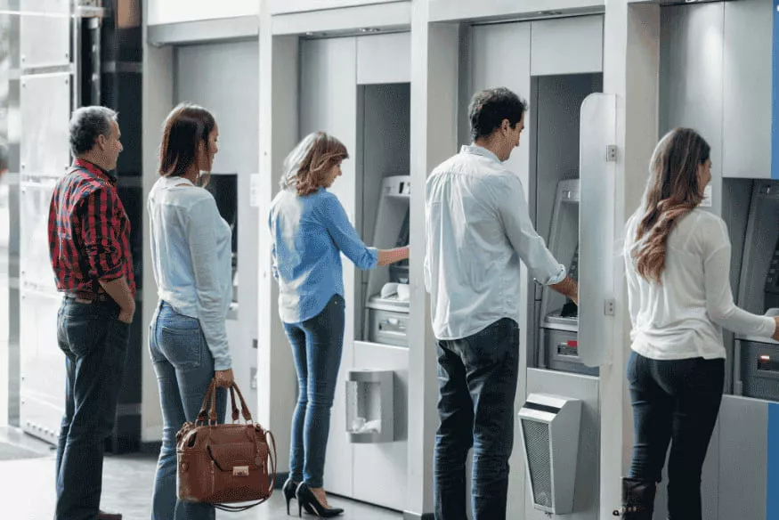 Persone in fila agli sportelli bancomat: perché il risparmio automatico aiuta a evitare prelievi e spese impulsive.