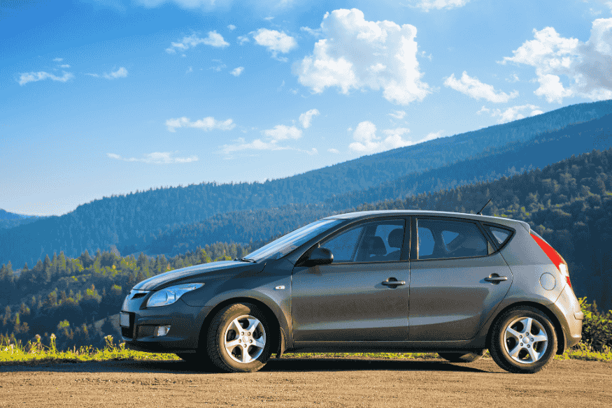 Carro hatch cinza em estrada de terra com vista montanhosa, representando veículos compactos