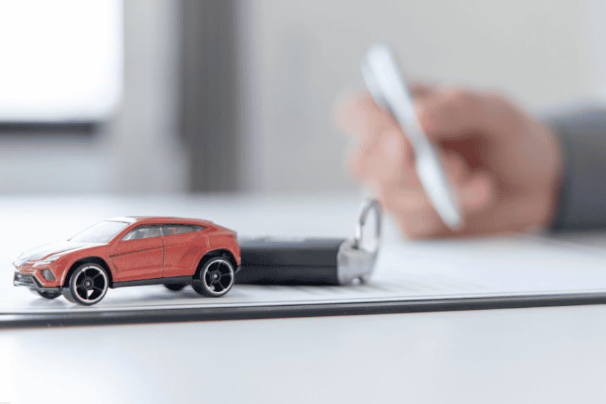 Carro em miniatura e chave de veículo sobre documento assinado, simbolizando aquisição por financiamento