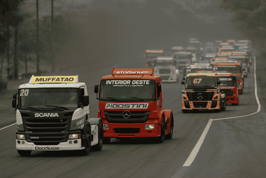 Caminhões da Fórmula Truck acelerando lado a lado em uma reta com fumaça ao fundo