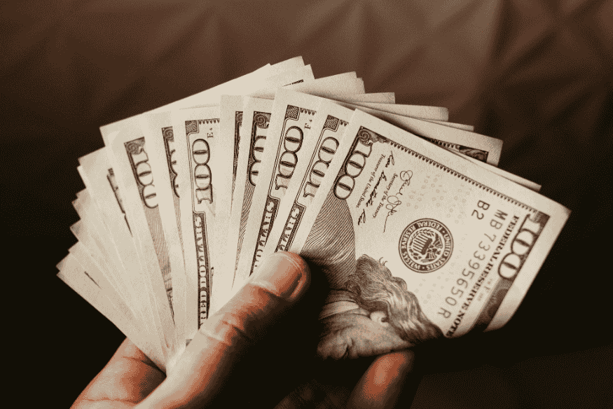 Mão segurando cédulas de cem dólares em leque, destacando o poder de compra em moeda estrangeira