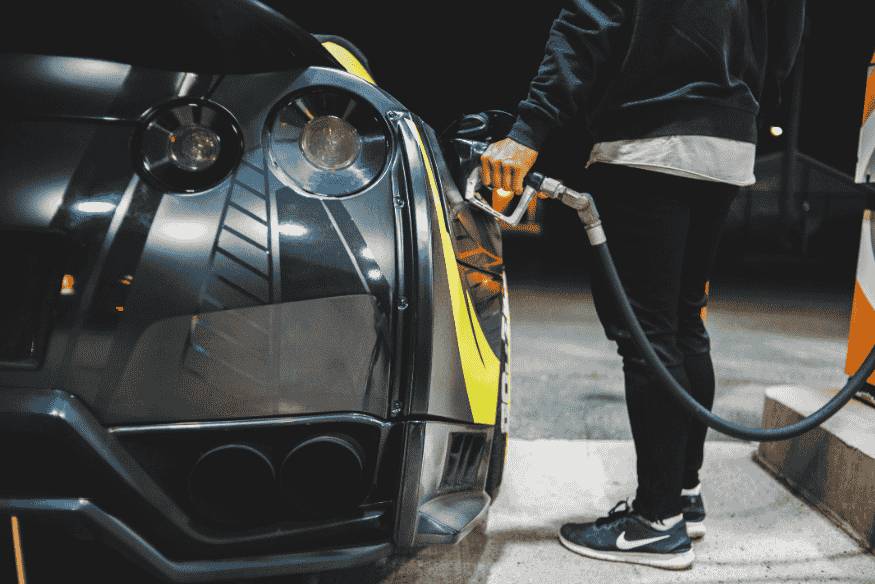 Pessoa abastecendo um carro esportivo preto em posto de gasolina à noite