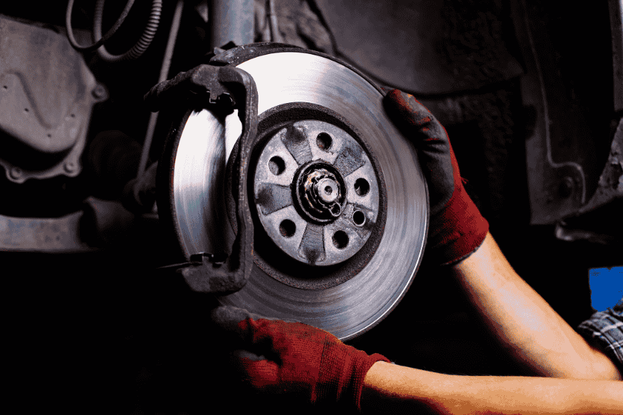 Técnico automotivo retirando disco de freio usado para manutenção ou substituição.
