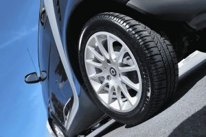 Pneu de perfil esportivo em carro compacto com rodas de liga leve, ideal para uso urbano.