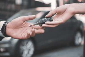 Pessoa entregando a chave do carro a outra em ambiente externo, representando finalização de compra.