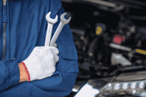 Técnico de oficina segurando duas chaves fixas com motor desfocado ao fundo.