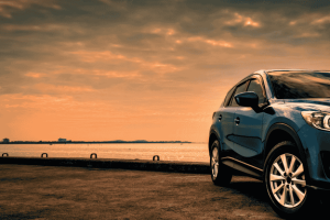 SUV azul estacionado em frente ao mar ao entardecer, com céu alaranjado.