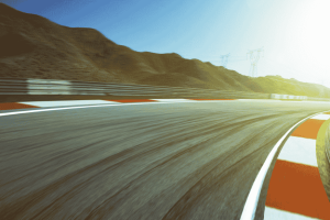 Curva acentuada de pista de corrida com paisagem montanhosa ao fundo e luz solar intensa