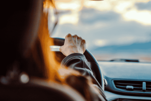Pessoa dirigindo com firmeza ao entardecer, com foco na mão sobre o volante.