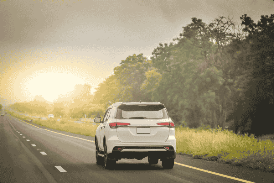 SUV branco percorrendo estrada ao entardecer, cercado por vegetação e céu dourado.